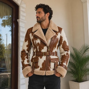 May include: A brown and white cow-print jacket featuring a wide lapel with tan faux fur lining, a gold-tone asymmetrical zipper closure, a matching waist belt with a gold buckle, two front flap pockets with tassels, and tan faux fur cuffs.