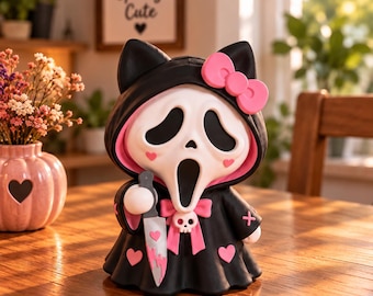 Puede incluir: Una figura de un personaje con una túnica negra con capucha, orejas de gato, un lazo rosa y corazones rosas. El personaje tiene una máscara blanca con aberturas negras para los ojos y la boca, y sostiene un cuchillo plateado con manchas de sangre rosa.