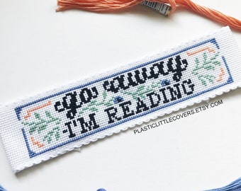May include: White cross-stitch bookmark with blue and green floral accents. The bookmark reads "Go Away I'm Reading".