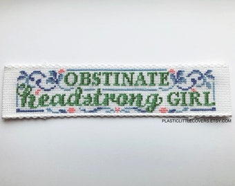 May include: White cross-stitch embroidery with blue and green floral accents. The text reads "Obstinate & Headstrong Girl".