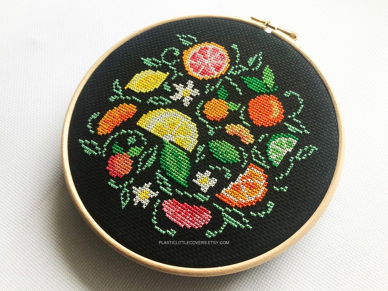May include: A black embroidery hoop with a colorful cross-stitch design of various citrus fruits, flowers, and leaves. The design includes lemons, limes, oranges, grapefruits, and white flowers.