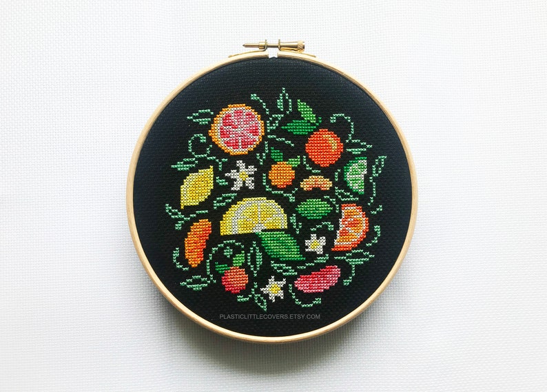 May include: A black embroidery hoop with a colorful cross-stitch design of citrus fruits, flowers, and leaves. The design includes lemons, limes, oranges, grapefruits, and white flowers. The text "PLASTICLITTLECOVERS.ETSY.COM" is at the bottom of the hoop.