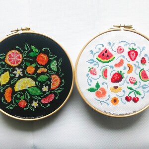 May include: Two embroidery hoops with black and white fabric. The black hoop features a colorful embroidery design of various fruits, including lemons, limes, oranges, and strawberries. The white hoop features a colorful embroidery design of watermelon, strawberries, peaches, and cherries.