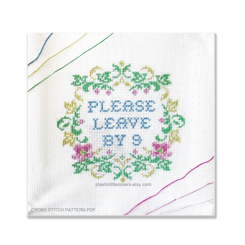 Peut inclure: Mod&egrave;le de point de croix pour une pancarte qui dit "Veuillez quitter avant 9 heures" avec une couronne de fleurs autour du texte. La couronne est verte, dor&eacute;e et rose.