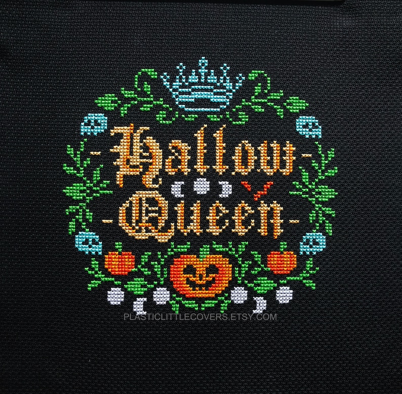 May include: Cross-stitch pattern featuring the text "Hallow Queen" in a gold color with a crown and pumpkins. The pattern is surrounded by green leaves and white moons.