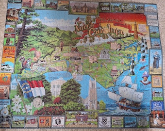 Könnte beinhalten: Ein Puzzle mit einer farbenfrohen illustrierten Karte von North Carolina und dem Text Historic North Carolina. Die Karte zeigt verschiedene Sehenswürdigkeiten, ein Segelschiff, Leuchttürme und kleine Vignetten historischer Orte am Rand.