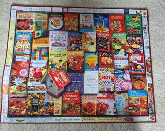Könnte beinhalten: Ein rechteckiges Puzzle mit einer Collage aus alten Betty Crocker Kochbuch-Covern. Das Bild zeigt verschiedene bunte kulinarische Buchtitel, Lebensmittelfotografien und eine zentrale Abbildung einer kleinen hausförmigen Rezeptbox.