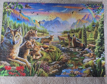 Könnte beinhalten: Ein rechteckiges Puzzle mit einer lebendigen Landschaft, die mehrere Wölfe im Vorder- und Hintergrund zeigt. Die Szene umfasst einen Wald, Berge, einen Bach mit Seerosen, einen Regenbogen sowie verschiedene Vögel und Schmetterlinge.