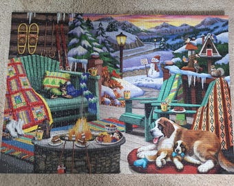 Könnte beinhalten: Ein Puzzle mit einer Winterszene auf einer Veranda, bestehend aus einer steinernen Feuerstelle, einer grünen Bank, einer bunten Decke, Schneeschuhen, einem Schneemann, einem Vogelhaus und einem Bernhardiner mit Welpen auf einer roten Matte.