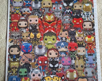 Könnte beinhalten: Ein fertiggestelltes Puzzle mit einer Collage aus zahlreichen Marvel-Charakteren als Funko Pop-Figuren in verschiedenen Farben und Posen. Unten in der Mitte ist der Text POP! MARVEL in einer weißen Sprechblase mit rotem Rand auf weißem Grund zu sehen.