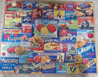 Könnte beinhalten: Ein rechteckiges Puzzle mit einer Collage aus alten Apfelkisten-Etiketten. Das farbenfrohe Design enthält verschiedene Markennamen wie Aurora, Rainier und Mustang sowie Illustrationen von roten und gelben Äpfeln, Apfelkuchen und Obstgarten-Szenen.