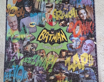 Könnte beinhalten: Ein rechteckiges Puzzle mit einer Collage aus Szenen der klassischen Batman-Fernsehserie. In der Mitte ist das Batman-Logo in Gelb und Schwarz zu sehen. Um das Logo herum befinden sich verschiedene Soundeffekte im Comic-Stil wie ZOPP, BIFF, SOCK, CRUNCH, BONK, POW, ZZZWAP, ZAP, EEEYOW, ARRRGH, CLANK und QUWEEKK.
