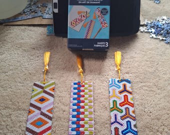 Könnte beinhalten: Ein Jonathan Adler x Michaels Diamond Art Lesezeichen-Set mit drei fertigen rechteckigen Lesezeichen. Jedes Lesezeichen zeigt ein einzigartiges, buntes geometrisches Muster aus kleinen Perlen und hat eine gelbe Quaste.
