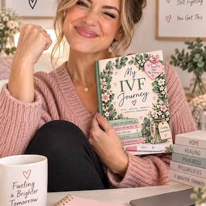 Op de afbeelding: Een boek getiteld My IVF Journey met bloemenillustraties, een roze hartvormig label en een zwangerschapstest. Daarnaast staat een witte mok met Fueling a Brighter Tomorrow, een roze notitieboek met Small Steps Big Dreams en een schaaltje met You Are So Brave.