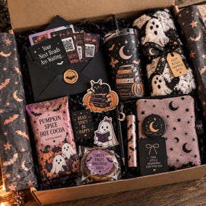 Könnte beinhalten: Eine Geschenkbox mit einem schwarzen Umschlag mit Fledermaussiegel, einem Becher mit Buch- und Monddruck, flauschigen Geistersocken, einer Packung Kürbisgewürz-Kakao, einem Notizbuch mit Mondmotiv, Aufklebern, einem Stift und einem Keks.