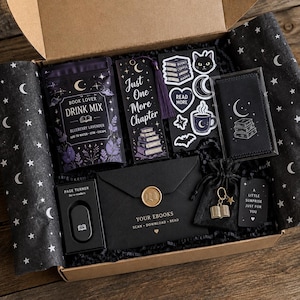 May include: A gift box containing a blueberry lavender drink mix, a bookmark with the text Just One More Chapter, a sheet of celestial stickers, a black case, a page turner, a black envelope with a gold seal, and a charm of an open book.