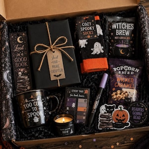 May include: A gift box containing a black wrapped book with a tag reading Just One More Chapter, a bookmark, ghost-patterned socks, Witches Brew hot cocoa, Wicked Caramel popcorn, a mug saying Too Cute To Spook, sticky tabs, a candle, and stickers.