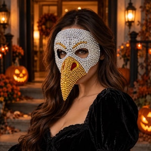 May include: A masquerade mask shaped like a bird head, fully covered in sparkling rhinestones. The upper portion features silver crystals, while the prominent beak is crafted from golden yellow rhinestones with dark accents around the eye openings.