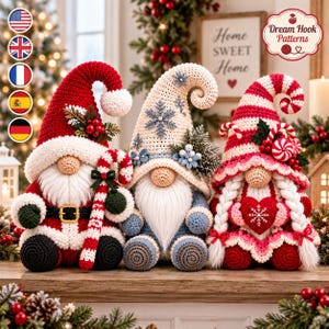 Pode incluir: Três figuras de gnomos de crochê sentadas lado a lado. O gnomo da esquerda usa um gorro vermelho com azevinho, o do centro tem um gorro creme com flocos de neve azuis e o da direita um gorro listrado de vermelho e branco com um coração e tranças.