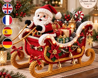 Puede incluir: Una figura de Papá Noel tejida a ganchillo sentada en un trineo rojo y dorado, lleno de cajas de regalo, un pequeño farol y un bastón de caramelo. El trineo está decorado con una flor de pascua roja, campanas doradas y luces LED cálidas.