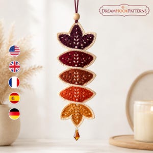 May include: A vertical hanging crochet decoration featuring five leaf-shaped segments in a gradient of colors from dark purple to bright yellow, finished with a cream-colored border, a wooden bead at the top, and a small amber-colored crystal at the bottom.
