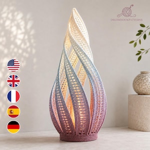 May include: A tall, flame-shaped decorative sculpture crafted from crocheted yarn. The piece features a vertical gradient color transition, starting with a light cream at the top, shifting through shades of blue, and ending in a deep mauve at the base.