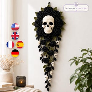 Puede incluir: Un adorno de pared con una calavera central de ganchillo color crema, rodeada por una corona de rosas negras de ganchillo y hojas verdes. De ella cuelgan enredaderas con rosas negras más pequeñas y calaveras en miniatura color crema.