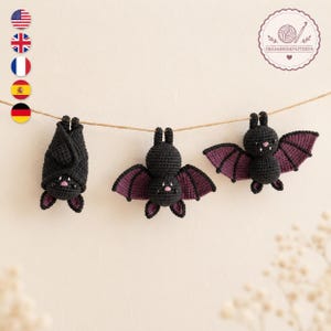 Pode incluir: Três morcegos pretos de crochê pendurados num fio castanho fino. Os morcegos apresentam o interior das asas em roxo escuro, pequenos narizes cor-de-rosa e minúsculas presas brancas. Um está enrolado, enquanto os outros dois estão abertos.