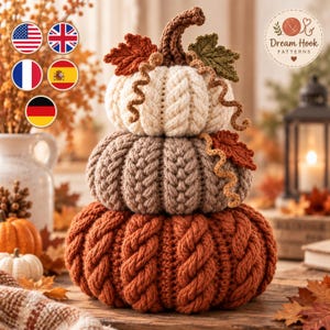 May include: A stack of three crocheted pumpkins in cream, light brown, and burnt orange, featuring cable knit textures and decorative crocheted leaves and vines. The image includes a logo with the text Dream Hook PATTERNS and five circular flag icons.