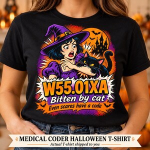 Könnte beinhalten: Ein schwarzes T-Shirt mit einer Grafik einer Person mit violettem Hexenhut, die von einer schwarzen Katze gebissen wird. Das Motiv zeigt ein Spukhaus, Fledermäuse und den Text W55.01XA Bitten by cat Even scares have a code in Orange und Gelb.