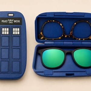 May include: A blue rectangular case shaped like a police box with the text POLICE PUBLIC CALL BOX, alongside an open blue case containing two pairs of glasses: one with a brown tortoiseshell frame and one with black frames and green lenses.