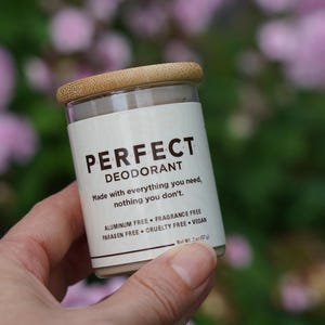 May include: A cylindrical deodorant container with a light wood-toned lid and a white label featuring the text PERFECT DEODORANT, Made with everything you need, nothing you don't, Aluminum Free, Fragrance Free, Paraben Free, Cruelty Free, Vegan, Net Wt. 2 oz.