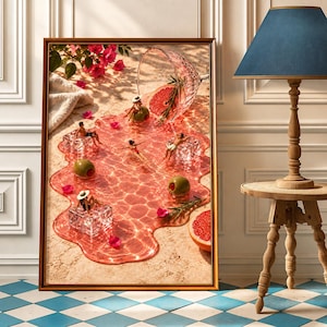May include: A framed wall art print depicting a spilled pink cocktail forming a pool on a sandy surface. Miniature figures lounge on ice cubes within the liquid, accompanied by green olives, a grapefruit slice, and scattered pink flower petals.