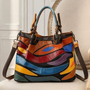 Puede incluir: Un bolso de mano de cuero multicolor con un diseño de parches de paneles curvos en tonos rojo, azul, amarillo, naranja, morado y verde sobre una base negra. El bolso incluye dos asas superiores, una correa de hombro marrón extraíble y herrajes.