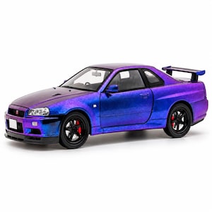 May include: A scale model of a Nissan Skyline GT-R R34 coupe featuring a metallic purple and blue colour-shifting paint finish. The car has black five-spoke wheels with visible red brake calipers, a rear spoiler, and clear headlights.