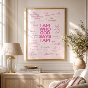 Könnte beinhalten: Ein gerahmter Kunstdruck mit hellrosa Hintergrund und dem fetten rosa Text I AM WHO GOD SAYS I AM, umgeben von kleineren rosa Phrasen wie I am fearfully wonderfully made, His masterpiece und more than a conqueror sowie biblischen Verweisen.