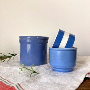 May include: Two blue ceramic containers with white stripes. The larger container has a lid. The smaller container is taller and has a wider opening.