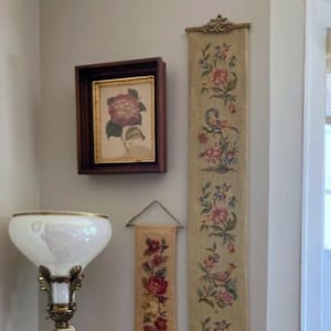 May include: A framed floral print and two decorative wall hangings with floral designs. A tall floor lamp with a white shade and ornate base is also visible. The wall hangings feature pink and red flowers.