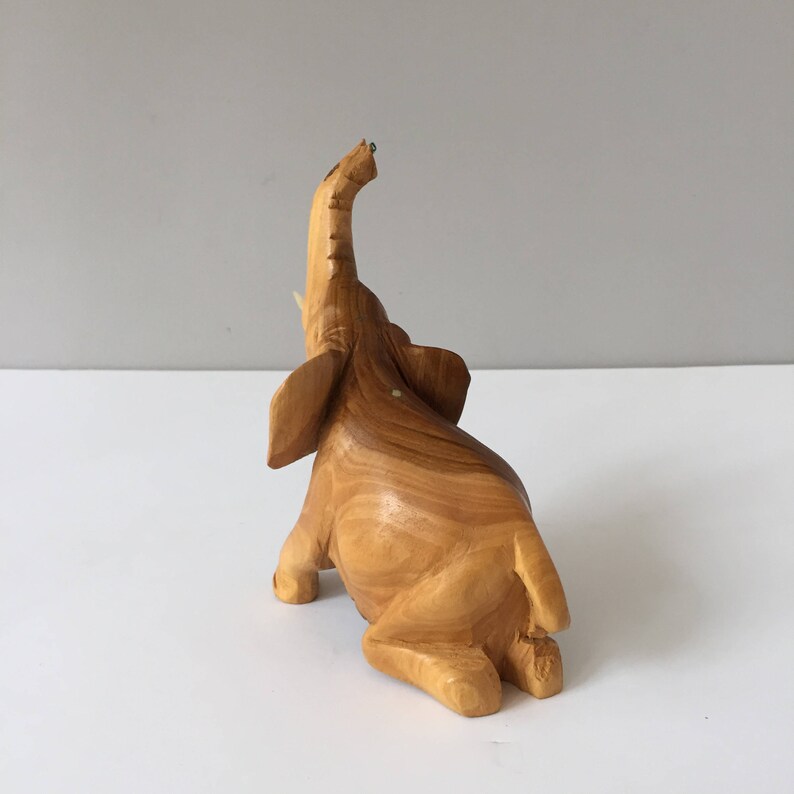 May include: A wooden elephant figurine with a raised trunk, carved from light brown wood with a natural wood grain finish.