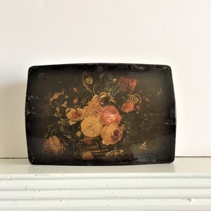 May include: A vintage wooden box with a floral design painted on the lid. The flowers are in shades of pink, yellow, and red, and the background is black. The box is rectangular and has a slightly rounded top.