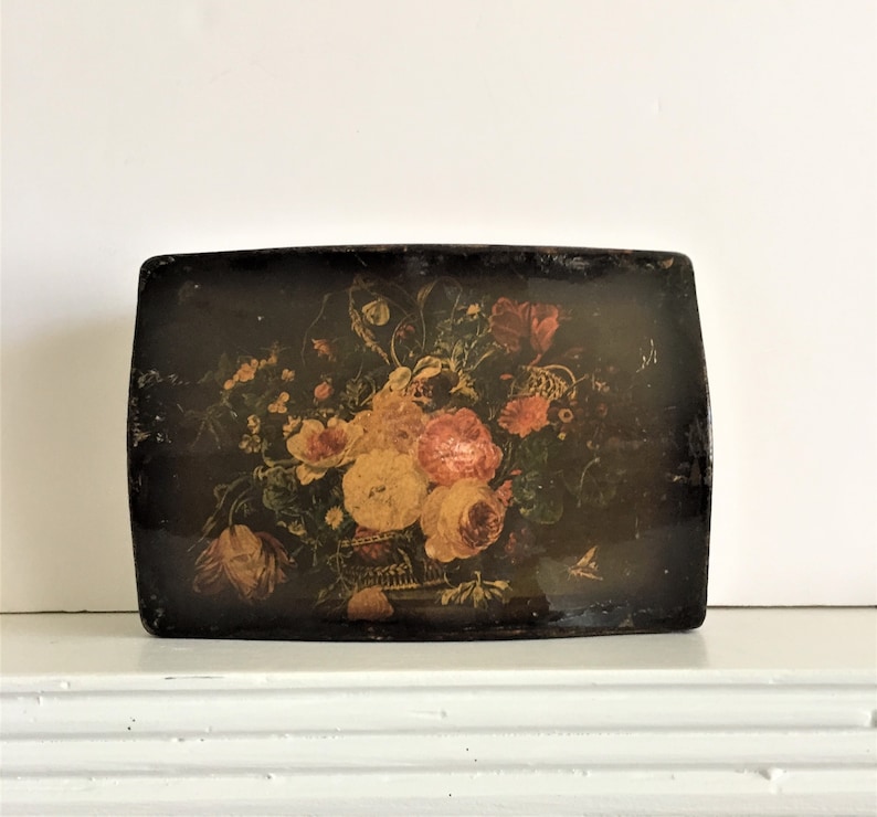 May include: A vintage wooden box with a floral design painted on the lid. The flowers are in shades of pink, yellow, and red, and the background is black. The box is rectangular and has a slightly rounded top.