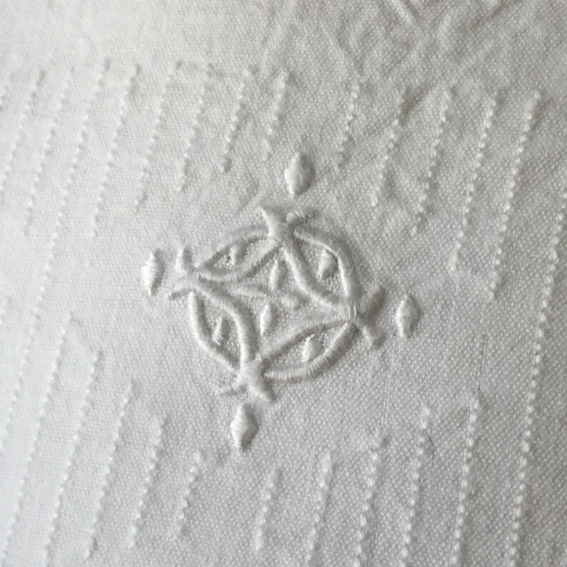 May include: White fabric with a delicate embroidered design in the center. The design is a circular pattern with intricate details.