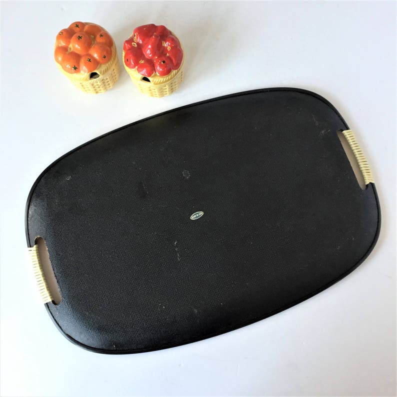 K&ouml;nnte beinhalten: Ein schwarzes Serviertablett mit einem geflochtenen Rand und einer leicht erh&ouml;hten Mitte. Zwei kleine Keramikk&ouml;rbe mit roten und orangefarbenen Fruchtmotiven stehen auf einer wei&szlig;en Oberfl&auml;che.