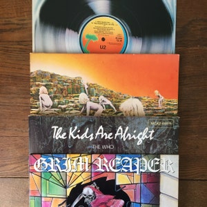 Puede incluir: Una pila de cuatro discos de vinilo. El disco superior es un disco de U2 con el t&iacute;tulo "Two Hearts Beat As One". El segundo disco es un disco amarillo y naranja con una escena de paisaje. El tercer disco es un disco negro con el t&iacute;tulo "The Kids Are Alright" de The Who. El disco inferior es un disco negro y colorido con el t&iacute;tulo "Grim Reaper".