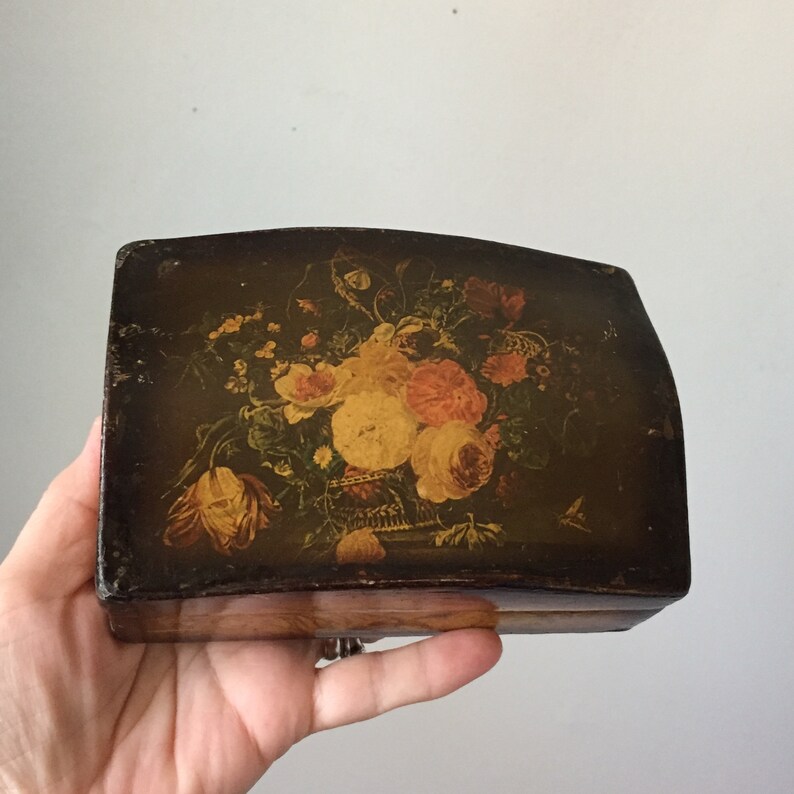 May include: A vintage wooden box with a hinged lid. The lid is decorated with a painted floral design featuring yellow, pink, and orange flowers on a dark brown background.
