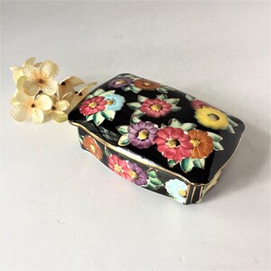 May include: A black rectangular trinket box with a gold trim and a floral design. The flowers are painted in shades of red, yellow, blue, and purple.