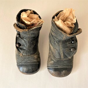 May include: A pair of black leather children's boots with button closures. The boots are worn and have a vintage look.