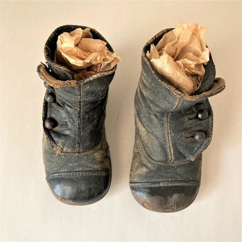 May include: A pair of black leather children's boots with button closures. The boots are worn and have a vintage look.