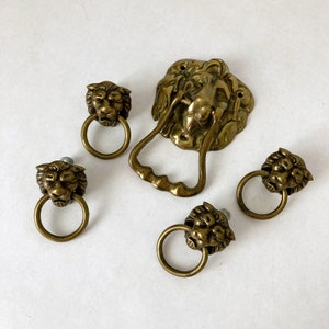 May include: Set of five brass lion head door knobs. The knobs are in the shape of a lion's head with a ring handle. One knob is larger and has a more ornate design.