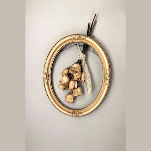 May include: A bouquet of dried roses hangs from a gold oval picture frame with a white background.